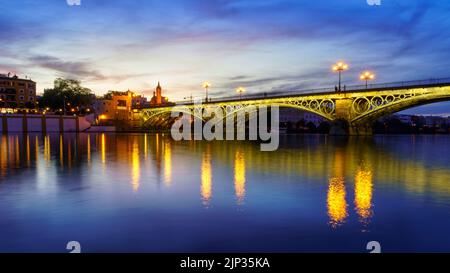 Pont de Triana à Séville au-dessus du fleuve Guadalquivir au coucher du soleil, avec des lumières reflétant dans l'eau du fleuve, une scène idyllique et charmante. Andalousie. Banque D'Images