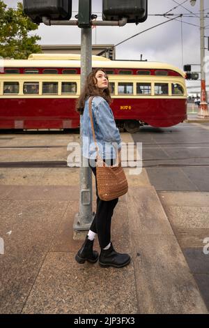 Portrait non posé d'une jeune femme qui attend de traverser une rue animée du centre-ville | Veste en Jean | San Francisco Wharf Banque D'Images