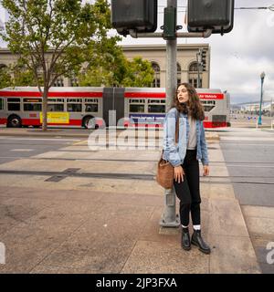 Portrait non posé d'une jeune femme qui attend de traverser une rue animée du centre-ville | Veste en Jean | San Francisco Wharf Banque D'Images