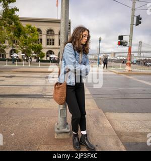 Portrait non posé d'une jeune femme qui attend de traverser une rue animée du centre-ville | Veste en Jean | San Francisco Wharf Banque D'Images