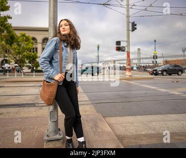 Portrait non posé d'une jeune femme qui attend de traverser une rue animée du centre-ville | Veste en Jean | San Francisco Wharf Banque D'Images