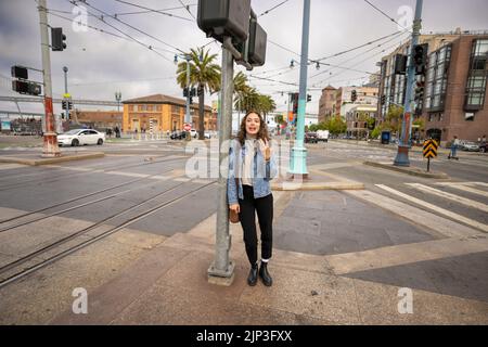 Portrait non posé d'une jeune femme qui attend de traverser une rue animée du centre-ville | Veste en Jean | San Francisco Wharf Banque D'Images