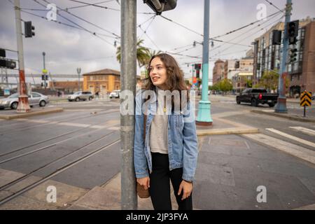 Portrait non posé d'une jeune femme qui attend de traverser une rue animée du centre-ville | Veste en Jean | San Francisco Wharf Banque D'Images