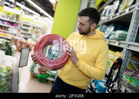 un jeune homme choisit un tuyau pour arroser un jardin et un potager dans un magasin d'amélioration de la maison Banque D'Images