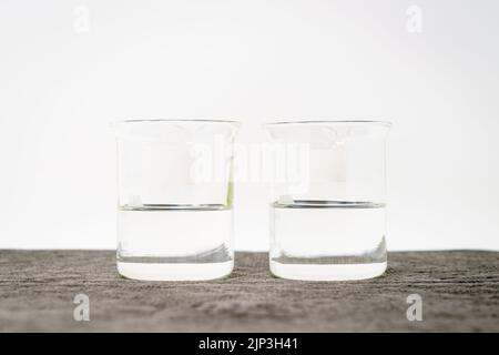 Deux béchers avec des liquides transparents et des étiquettes vierges sur fond blanc Banque D'Images