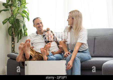 Chauffage électrique à la maison. Une jeune famille réchauffe ses mains gelées près d'un radiateur de chauffage Banque D'Images