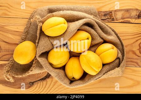 Plusieurs abricots jaune vif juteux à l'ananas avec un sac de jute sur une table en bois, macro, vue de dessus. Banque D'Images