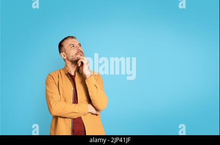 Homme mûr et réfléchi regardant de côté posant sur fond bleu Banque D'Images