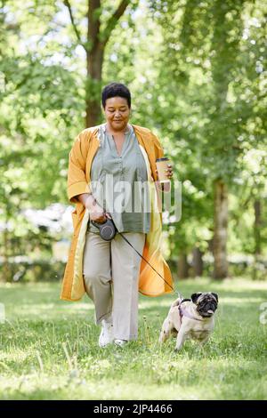 Portrait vertical en longueur de femme noire souriante marchant mignon chien dans le parc et appréciant le café Banque D'Images