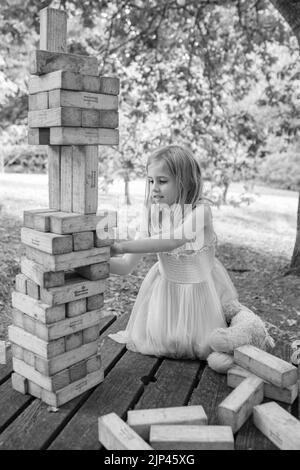 5yr vieille fille en robe rose et bleue jouant avec des blocs de bois dans un cadre de parc Banque D'Images