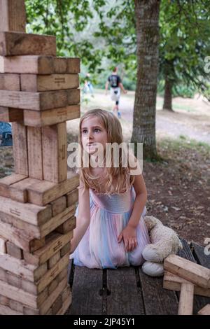 5yr vieille fille en robe rose et bleue jouant avec des blocs de bois dans un cadre de parc Banque D'Images