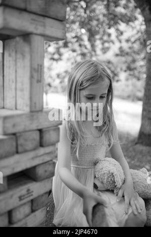 5yr vieille fille en robe rose et bleue jouant avec des blocs de bois dans un cadre de parc Banque D'Images