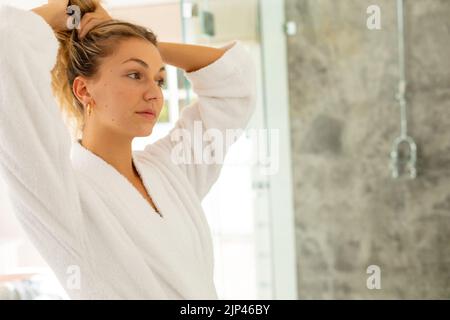 Bonne femme de race blanche portant une robe, nouant les cheveux dans la salle de bains Banque D'Images