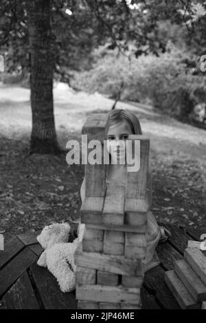 5yr vieille fille en robe rose et bleue jouant avec des blocs de bois dans un cadre de parc Banque D'Images