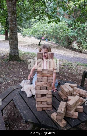 5yr vieille fille en robe rose et bleue jouant avec des blocs de bois dans un cadre de parc Banque D'Images