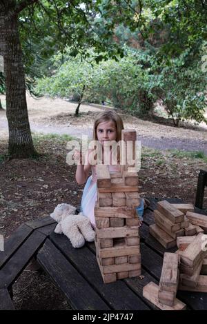 5yr vieille fille en robe rose et bleue jouant avec des blocs de bois dans un cadre de parc Banque D'Images