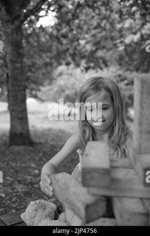 5yr vieille fille en robe rose et bleue jouant avec des blocs de bois dans un cadre de parc Banque D'Images