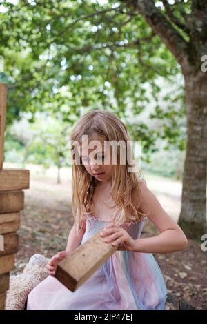 5yr vieille fille en robe rose et bleue jouant avec des blocs de bois dans un cadre de parc Banque D'Images