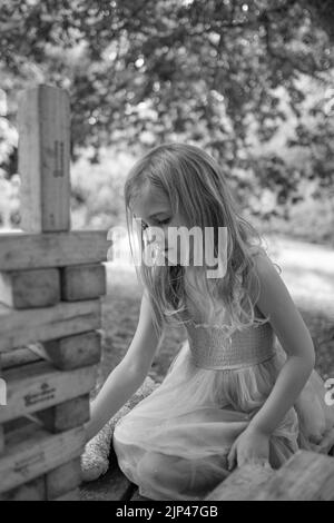 5yr vieille fille en robe rose et bleue jouant avec des blocs de bois dans un cadre de parc Banque D'Images