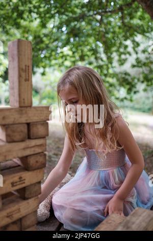 5yr vieille fille en robe rose et bleue jouant avec des blocs de bois dans un cadre de parc Banque D'Images