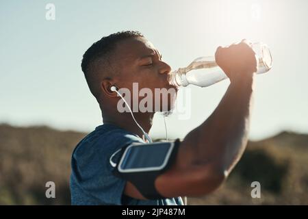 Courir m'a fait chaud, l'eau me refroidit. Un jeune homme charmant qui fait une pause et qui boit de l'eau à l'extérieur. Banque D'Images
