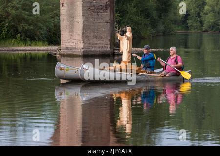 Le voyage de notre-Dame des eaux et du Wye. Une statue en bois nouvellement sculptée de la Vierge Marie est en train d'être flottée à 75 milles le long de la rivière Wye, de Hay-on-Wye à Monmouth, du 15th au 19th août 2022. Le sculpteur, Philip Chatfield (en rose) et un ami, Callum Bulmer (en bleu), font le voyage pour faire prendre conscience des niveaux élevés de pollution dans le Wye, l'un des fleuves les plus importants et les plus beaux de Grande-Bretagne. On les voit ici passer sous l'ancien pont à Bredwardine, Herefordshire. Banque D'Images