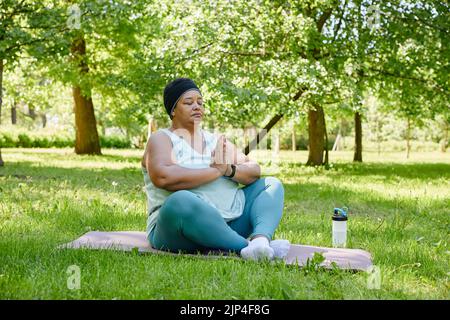Portrait en longueur de femme noire en surpoids faisant du yoga à l'extérieur et méditant avec les yeux fermés dans le parc, l'espace de copie Banque D'Images