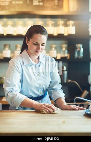 Le café reste impeccable sous sa direction. Une jeune femme nettoie un comptoir dans son café. Banque D'Images