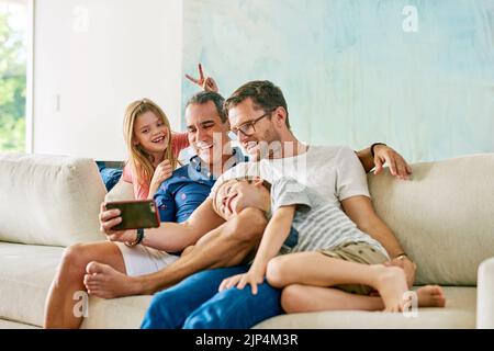 Prendre des selfies stupides sur le canapé. Une famille affectueuse de quatre personnes prenant des selfies sur le canapé à la maison. Banque D'Images