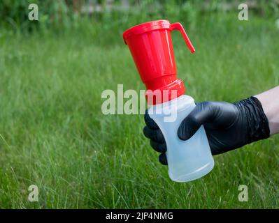 Main dans un gant en nitrile noir tenant une tasse à trempette pour la désinfection de la vache sur fond d'herbe verte, espace de copie. Pratique de traite Banque D'Images