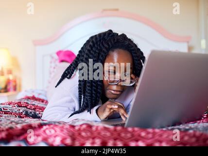 En savoir plus sur la technologie. Une adorable petite fille utilisant un ordinateur portable tout en étant allongé sur son lit dans sa chambre. Banque D'Images