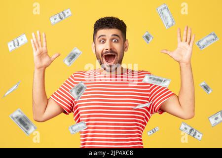 Oh mon dieu, wow. Portrait de l'homme émerveillé regardant l'appareil photo avec les grands yeux et la bouche ouverte, absolument choqué de la pluie d'argent tombant de haut. Intérieur isolé sur fond jaune Banque D'Images