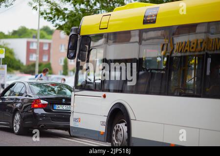 Un bus jaune et une voiture BMW devant lui conduisant dans une rue en journée à Geilenkirchen, en Allemagne Banque D'Images