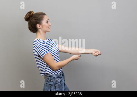 Portrait d'une femme forte et ambitieuse portant un T-shirt prétendant tirer la corde invisible, concept de travail dur, effort et les efforts à des réalisations. Prise de vue en studio isolée sur fond gris. Banque D'Images