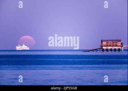 Esturgeon pleine lune se levant au-dessus du hangar de bateau et de la jetée Banque D'Images