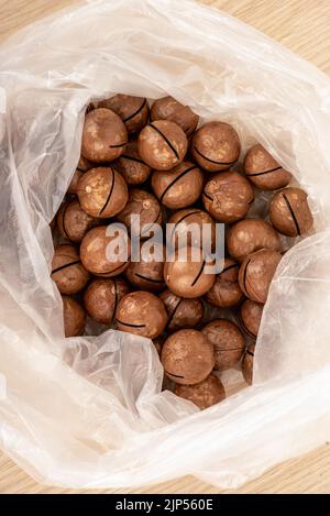 Vue de dessus des noix de macadamia non pelées dans un sac en plastique sur une table en bois. Le macadamia est un genre de plantes ligneuses de la famille des Proteaceae. Banque D'Images