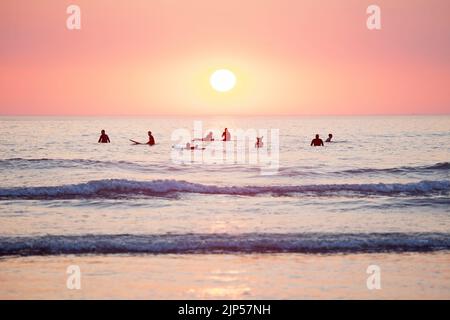 Surfeurs attendant les vagues au coucher du soleil. Cornouailles, Angleterre Banque D'Images