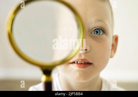 Visages d'un garçon tenant une loupe dans sa main et regardant joyeusement dans la caméra à travers elle. Gros plan. Banque D'Images