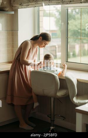 Maman nourrit le porridge garçon avec une cuillère d'une assiette. Nourriture Banque D'Images