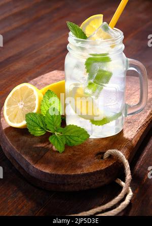 Limonade avec glace en verre avec poignée et paille à boire avec baume de citron et citron sur table et planche rustiques en bois Banque D'Images