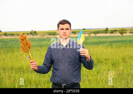Recentrer le jeune homme portant le drapeau ukrainien et les épis de blé de blé attachés et le drapeau sur le fond de la nature du pré. Drapeau de l'Ukraine. Liberté. Hors foyer Banque D'Images