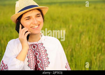 Recentrer le portrait de la jeune femme ukrainienne. Arrière-plan nature prairie. Une fille ukrainienne souriante parle le téléphone. Santé mentale. Assistance téléphonique. Hors foyer Banque D'Images