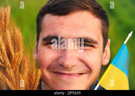 Recentrer le portrait du jeune homme ukrainien. Bouquet d'épillets dorés mûrs de blé attachés sur le fond de la nature du pré. Drapeau de l'Ukraine. Ukrainien souriant Banque D'Images