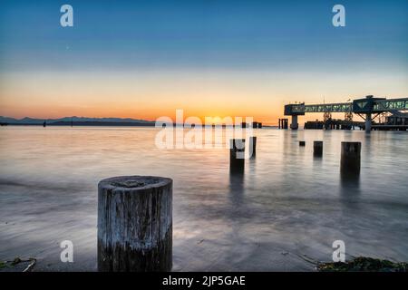 Un beau coucher de soleil sur l'océan avec des briseurs de vagues en bois dans l'eau, un pont moderne en arrière-plan et un ciel bleu jaune Banque D'Images