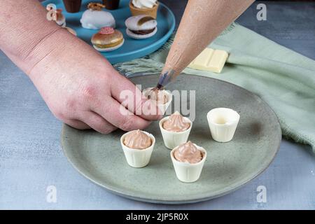 Confiseur remplissant de petites tasses de chocolat blanc avec mousse de chocolat au lait vue latérale. Banque D'Images