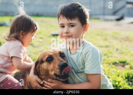 Vue de face portrait de deux enfants jouant avec un chien de compagnie dans la cour. Bonne famille, enfance. Banque D'Images