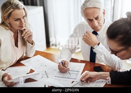 Tout semble aller en conséquence. Un groupe d'architectes travaillant ensemble sur les plans d'une maison autour d'une table à l'intérieur d'un bâtiment. Banque D'Images