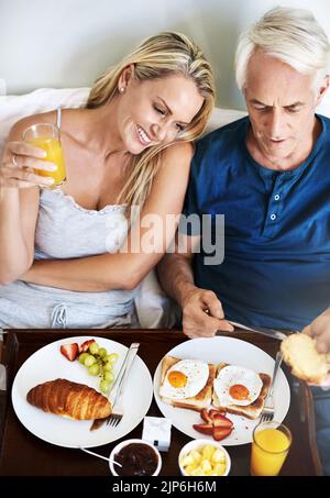 Réveillez-vous ensemble pour une journée parfaite. Un couple affectueux et mature qui prend son petit déjeuner au lit à la maison. Banque D'Images