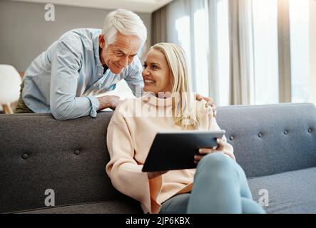 Hé miel, jetez un coup d'œil à cela. Un couple mature utilisant une tablette numérique sur le canapé à la maison. Banque D'Images