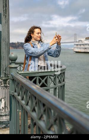 Jeune femme sur la jetée surplombant la baie de San Francisco prendre des photos avec un smartphone Banque D'Images